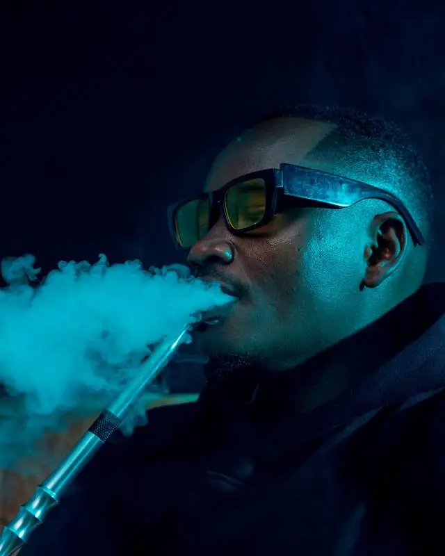 Cliente exhalando humo de hookah bajo luz azul en un lounge nocturno de Cancún