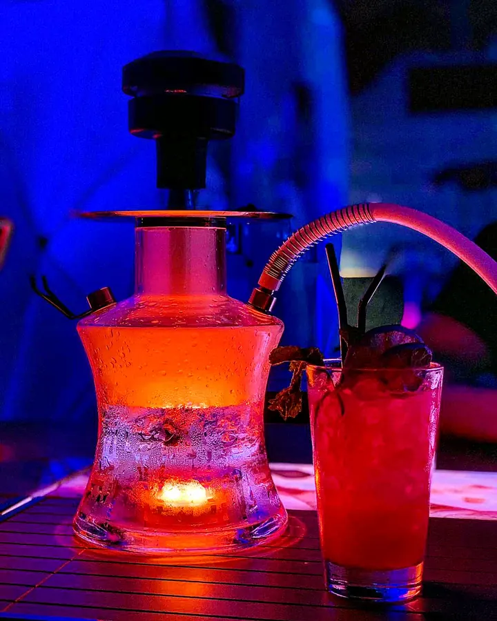 Hookah iluminada con coctel en mesa de lounge nocturno